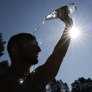 Ein Mann kühlt sich bei sommerlichen Temperaturen ab, indem er sich Wasser aus einer Flasche über den Kopf schüttet.