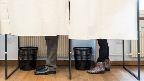 Zwei Personen in zwei Wahlkabinen (Symbolbild)