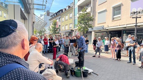 Ein Mann mit Kippa und viele Passanten stehen in einer Fussgängerzone und verlegen goldfarbene Steine im Boden. In der Innenstadt wurden insgesamt 20 Stolpersteine für verfolgte Juden aus dem Nationalsozialismus verlegt.