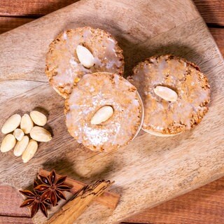 Nach dem Backen liegen die Lebkuchen auf einem Holzbrett. Die Elisenlebkuchen sind wie im Rezept beschrieben mit Zuckerguss glasiert und Mandeln dekoriert. 
