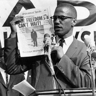 Malcolm X  hält am 6. August 1963 während einer Veranstaltung in New York eine Rede und hält vor dem Publikum eine Zeitung hoch. Mit seinem Kampfgeist und Einsatz für die Rechte der Schwarzen inspirierte er zahlreiche Bewegungen, die sich für die Rechte der Schwarzen in den USA einsetzten, zuletzt die Black-Lives-Matter-Bewegung.