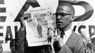 Malcolm X  hält am 6. August 1963 während einer Veranstaltung in New York eine Rede und hält vor dem Publikum eine Zeitung hoch. Mit seinem Kampfgeist und Einsatz für die Rechte der Schwarzen inspirierte er zahlreiche Bewegungen, die sich für die Rechte der Schwarzen in den USA einsetzten, zuletzt die Black-Lives-Matter-Bewegung.