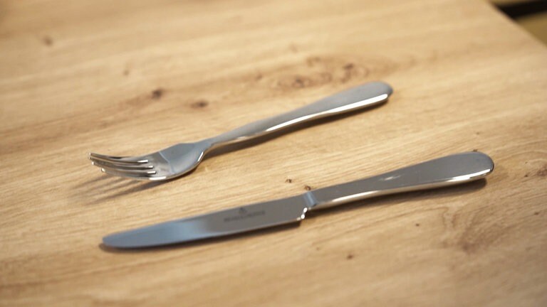 Auf einem Holztisch liegen Messer und Gabel. Das Besteck ist schwerer als gewöhnliches, da es älteren Menschen mit zittrigen Händen helfen soll.