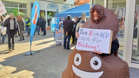 Mann protestiert in Neustadt in einem Kostüm, das wie ein Kackhaufen aussieht