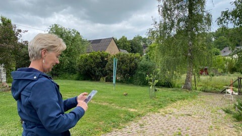 Claudia Diesler steht mit ihrem Smartphone in der Hand im Garten