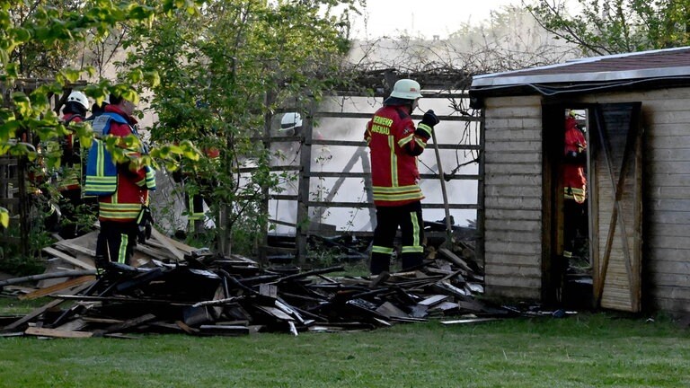 Feuerwehrleute vor einer zerstörten Holzhütte. Die Gartenhütten lagen nicht direkt nebeneinander. Die Polizei geht daher von Brandstiftung aus bei dem Brand in der Kleingartenanlage in Langenau.