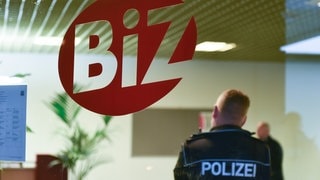 Ein Polizist steht im Gebäude der Agentur für Arbeit vor einem Logo des Berufsinformationszentrums (BiZ).