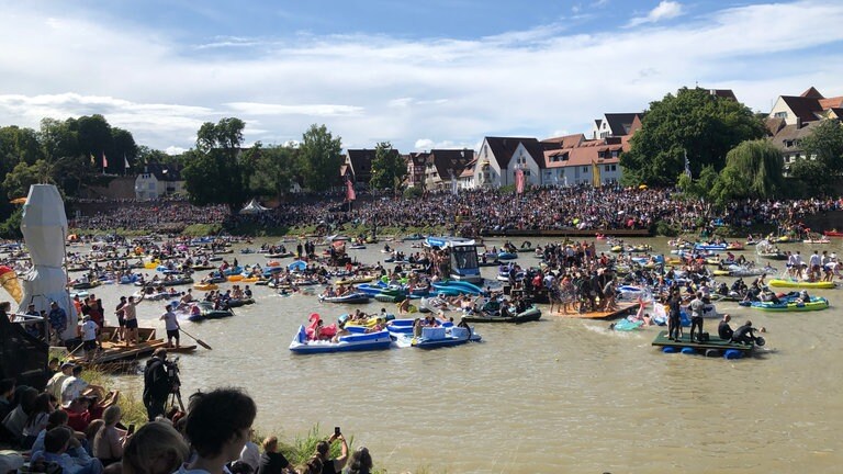 Die Donau ist voll mit wilden Nabadern auf ihren Gummibooten. Tausende Zuschauende haben es sich an beiden Ufern bequem gemacht. 