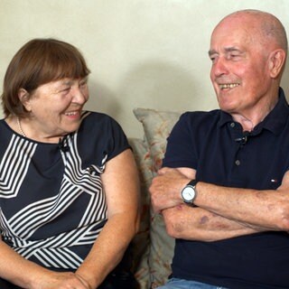 Uli und Gabi sitzen auf einem Sofa und lächeln sich an.