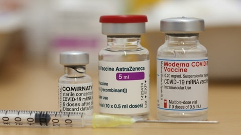 Ampullen mit den Corona-Impfstoffen von Biontech Comirnaty, Astrazeneca und Moderna: Erfolge und Rückschläge bei der Impfstoff- und Medikamenten-Entwicklung haben die Corona-Krise im Jahr 2021 geprägt; vor den Ampullen liegt eine Spritze