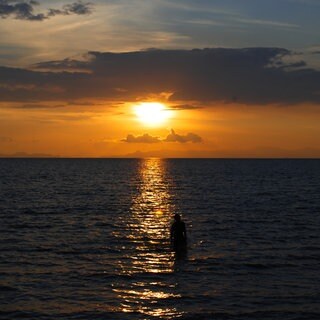 Eine Person steht im Meer während die Sonne untergeht