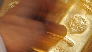 Symbolbild: Hand greift nach Goldbarren