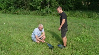 Michael steht mit seinem Partner Paddy auf einer Wiese und kniet sich zu einem Vogel hin.