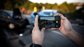 Symbolbild eines Gaffers Schaulustigen der mit dem Handy ein Bild eines Verkehrsunfalls macht.