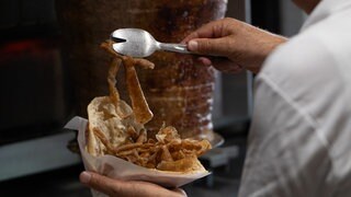Ein Mann füllt ein Fladenbrot mit Fleisch von einem Dönerspieß. Der Spieß wurde von der Firma Birtat produziert.