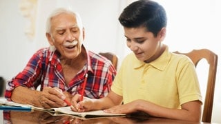 Ein älterer Mann hilft einem Jungen bei den Hausaufgaben: Persönliche Mentorinnen oder Mentoren sollen Kindern aus sogenannten bildungsfernen Schichten helfen, ihre Ziele zu erreichen. Die Angebote reichen von Hausaufgabenhilfe bis zu Ausflügen in den Zoo oder ins Museum.