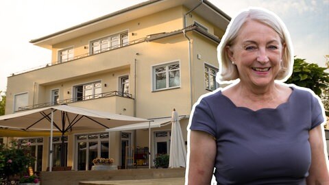 Blonde mittelalte Frau vor riesiger Fertighaus-Villa