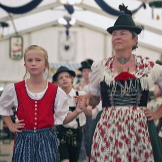Eine Frau und ein Mädchen im Dirndl marschieren im Festzelt ein
