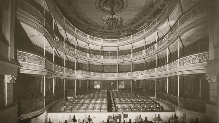 Ein Zuschauerraum mit Bühne und Kronleuchter, historische Aufnahme