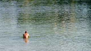 Ein Mann geht zum Schwimmen in den Vogelstangsee in Mannheim. Am Donnerstag werden hohe Temperaturen erwartet.