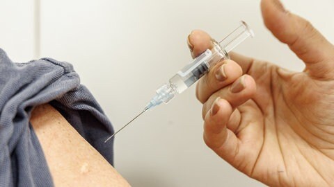 Eine Impfspritze wird in den Arm des Patienten geführt.