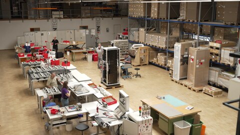 Der Blick in eine Arbeitshalle der Elektrofirma Intec in Besigheim mit Tischen, Kartons, Mitarbeitern und Elektrogeräten. 