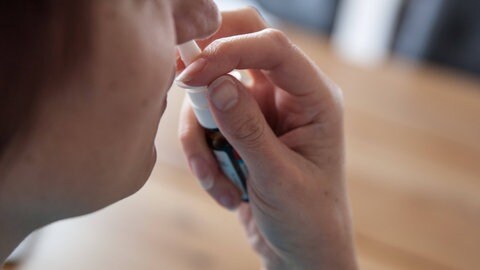 Frau verabreicht Nasenspray gegen Pollenallergie - das Spray hilft bei einer verstopften Nase durch Heuschnupfen.