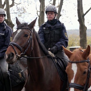 Polizeihauptmeisterin Sarah Heid sitzt in Uniform auf dem Pferd Finn. Links und rechts von ihr sitzen weitere uniformierte Kollegen auf Pferden.