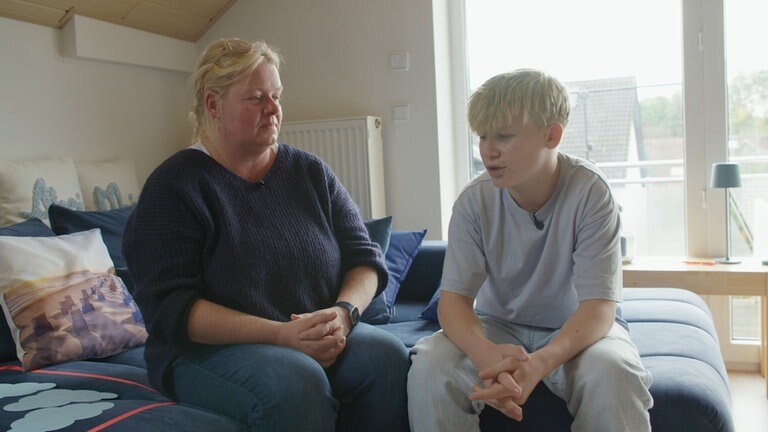 Eine blonde Frau und ihr Sohn sitzen auf einer blauen Couch mit Kissen und reden. 