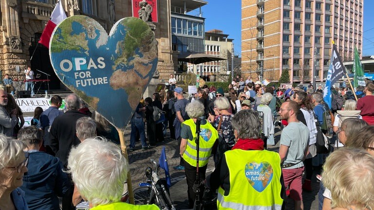 Teilnehmende der Demonstration von Fridays for Future in Freiburg. Ein Teilnehmer hält ein herzförmiges Schild mit Weltkarte hoch, auf der Opas for Future steht.