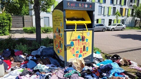 Offenbar überfüllter Altkleidercontainer mit ringsherum verstreuten Altkleidern in Landau. 