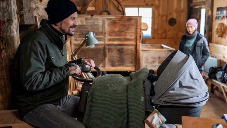 Constantin (Robert Besta) sitzt vor Konrads Kinderwagen, im Hintergrund sitzt Sophie (Janina Flieger)