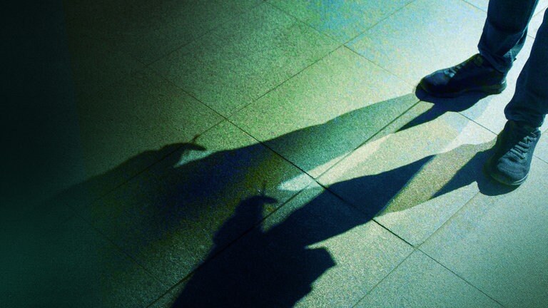 Der Tod - Im Anschnitt sind die Beine eines Mannes zu sehen; seine Erscheinung ist durch lange, ins Bild ragende und sich überlappende Schatten zu erkennen.