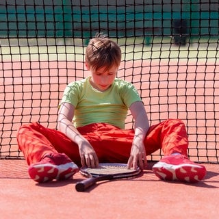 Der Junge hat den Tenniswettbewerb verloren. Das Kind sitzt mit einem Schläger am Netz.   