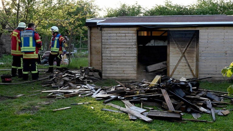 Feuerwehrleute vor einer zerstörten Holzhütte. Nach den Bränden in der  Kleingartenanlage in Langenau ermittelt die Polizei wegen Brandstiftung. 