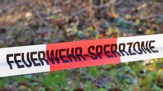 Ein rot-weißes Absperrband der Feuerwehr am Waldrand.