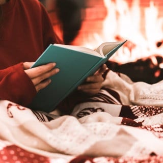 Frau liest ein Buch vor dem Kamin