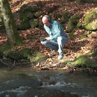 Dre. Becker mit Aufnahmegerät an einem Waldbach