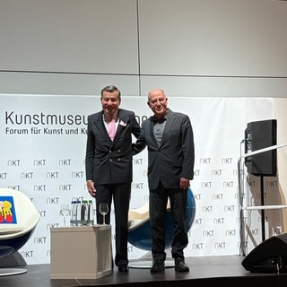 Wolfgang Grupp und Gregor Gysi nach dem Gespräch, Arm in Arm auf der Bühne.