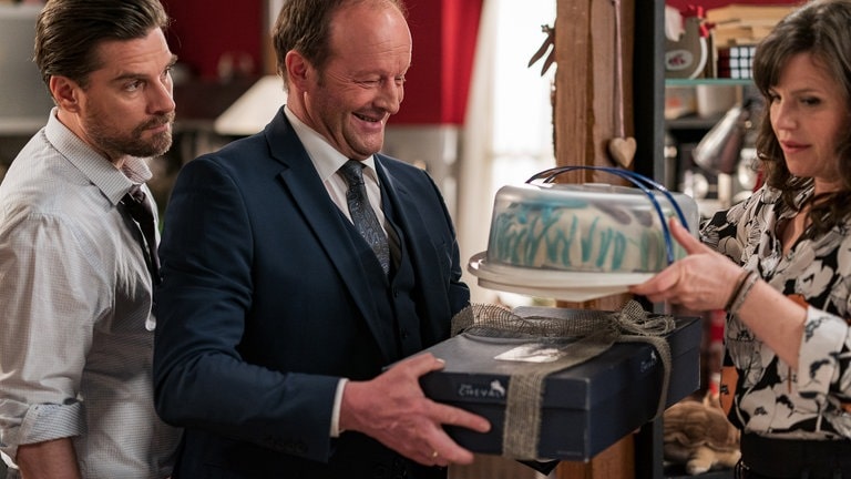Andreas und Eva bestaunen Bernds Kuchen, den er in den Händen hält