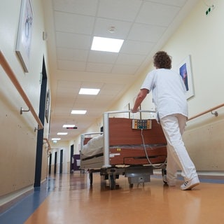Ein Pfleger schiebt ein Bett in einem Krankenhausflur. Der rheinland-pfälzische Gesundheitsminister Hoch (SPD) hat am Donnerstag den Fahrplan für die Umsetzung der Krankenhausreform vorgestellt. 
