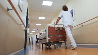Ein Pfleger schiebt ein Bett in einem Krankenhausflur. Der rheinland-pfälzische Gesundheitsminister Hoch (SPD) hat am Donnerstag den Fahrplan für die Umsetzung der Krankenhausreform vorgestellt. 