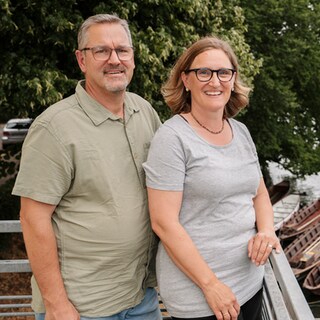 Ulrike und Christoph Brandner stehen auf einem Balkon. Beide lächeln in die Kamera. 