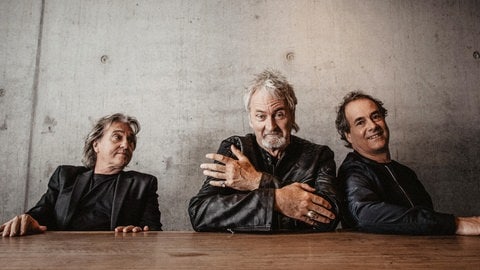 Die drei Bandmitglieder von Frontm3n sitzen zusammen an einem Tisch und schauen in die Kamera