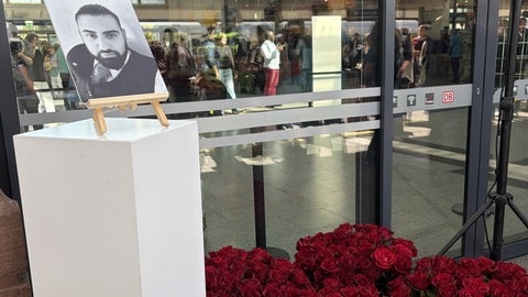 Ein Bild des getöteten Zugbegleiters Serkan Çalar ist am Mannheimer Hauptbahnhof aufgestellt worden. Darunter liegen rote Rosen.