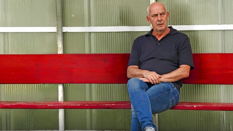 Mario Basler sitzt auf einer roten Bank am Spielfeldrand.