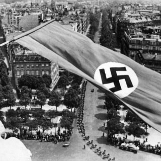 Die Fahne des Deutsches Reiches weht auf dem Arc de Triomphe in Paris. Dahinter zwei Straßen von Paris und durch sie marschierende Truppen.