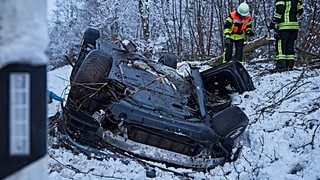 In winterlicher Landschaft liegt ein Auto im Straßengraben auf dem Dach. Feuerwehrleute sind vor Ort. 