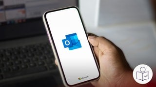Eine Hand halt ein Handy fest. Auf dem Bildschirm sieht man ein Logo. Es ist das Logo von dem E-Mail-Programm Outlook. Im Hintergrund steht ein Laptop. Rechts das SWR Logo für Leichte Sprache. 