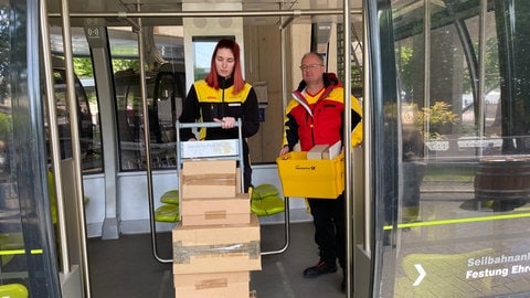Zwei Paketzusteller demonstrieren, wie der Transport von Paketen mit der Koblenzer Seilbahn ablaufen könnte. 